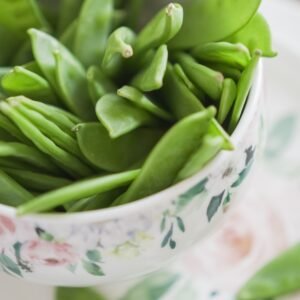 a cup of mange tout. The mange tout are vibrant green and flat with the pods just slightly visible