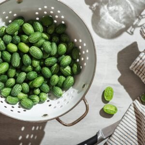 a colander full of small green cucamelons that look like miniature watermelons